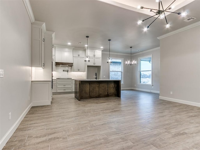 kitchen with cooktop, pendant lighting, a center island with sink, a notable chandelier, and white cabinets