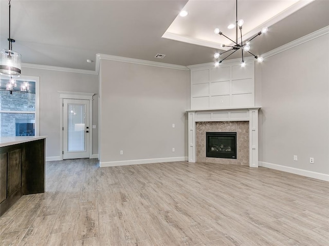 unfurnished living room with light hardwood / wood-style floors, ornamental molding, a fireplace, and a chandelier