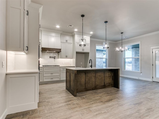 kitchen with gas cooktop, sink, decorative light fixtures, light hardwood / wood-style flooring, and an island with sink