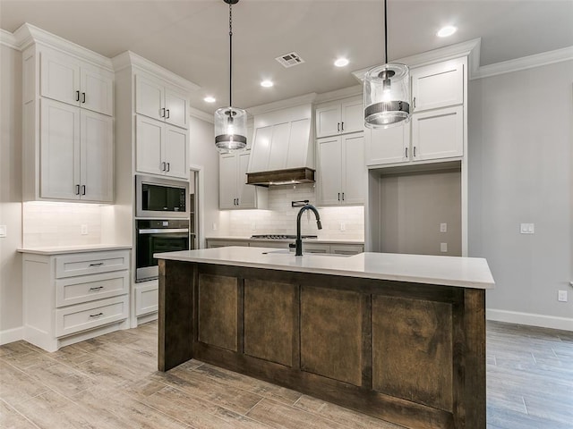 kitchen featuring pendant lighting, custom exhaust hood, stainless steel oven, built in microwave, and an island with sink