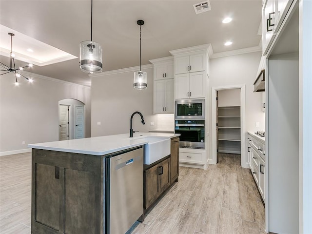 kitchen featuring pendant lighting, an island with sink, appliances with stainless steel finishes, light hardwood / wood-style floors, and white cabinetry