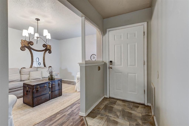 entryway with baseboards, a textured ceiling, wood finished floors, and a notable chandelier