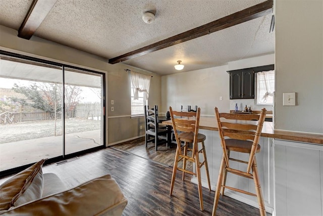 dining space featuring plenty of natural light, a textured ceiling, dark wood-type flooring, and beam ceiling