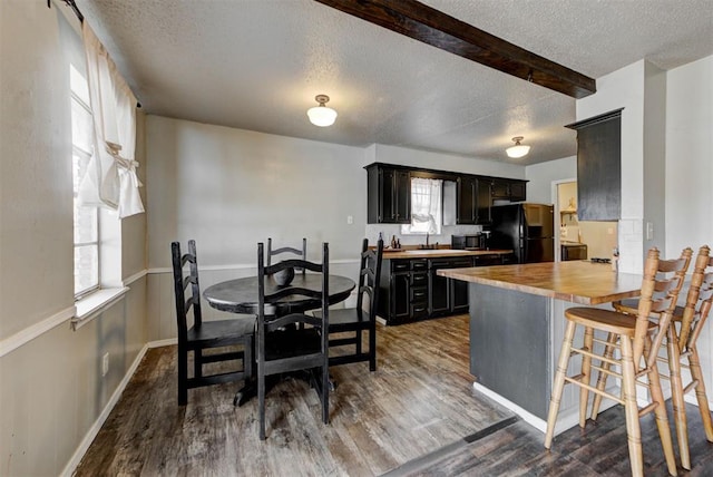 kitchen featuring dark cabinets, a breakfast bar, wood finished floors, wooden counters, and freestanding refrigerator