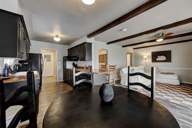 dining room with arched walkways, a textured ceiling, a ceiling fan, wainscoting, and beamed ceiling