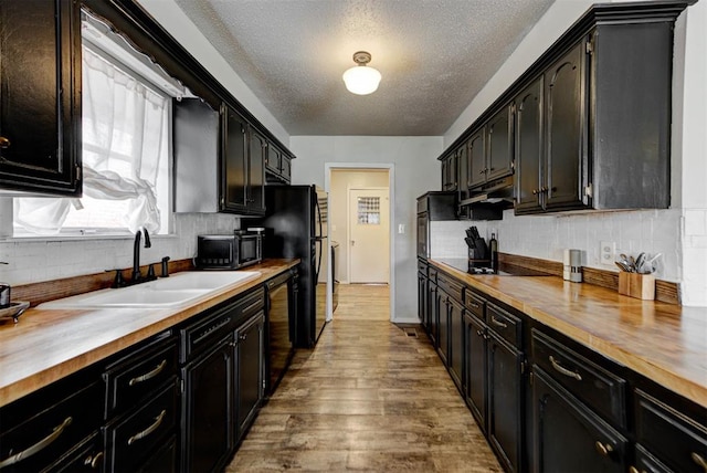 kitchen featuring wooden counters, black appliances, backsplash, and a sink