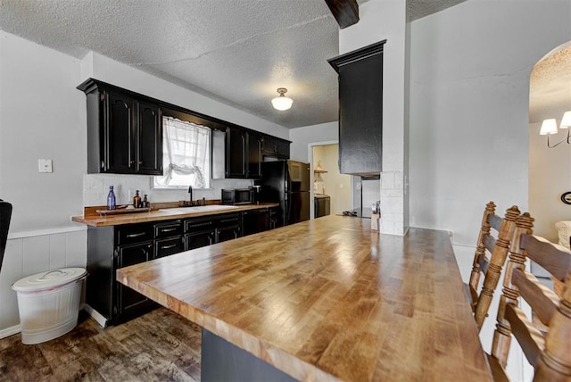 kitchen featuring dark cabinets, freestanding refrigerator, a sink, and a textured ceiling