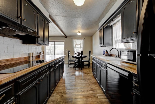 kitchen featuring dark wood-style flooring, a sink, a textured ceiling, under cabinet range hood, and black appliances