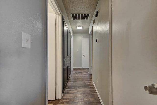 hallway with dark wood-style floors, baseboards, visible vents, and a textured ceiling