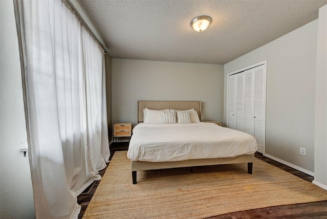 bedroom featuring a textured ceiling, a closet, wood finished floors, and baseboards