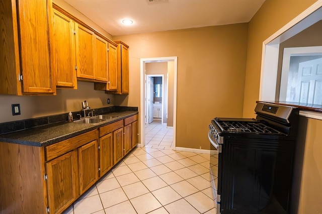 kitchen featuring gas range, light tile patterned floors, dark stone countertops, and sink