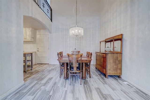 dining room featuring light wood-type flooring, a high ceiling, and an inviting chandelier