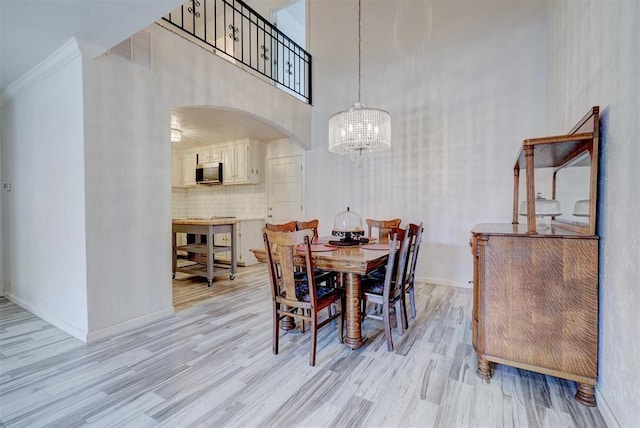 dining room featuring a high ceiling, light wood-type flooring, ornamental molding, and a notable chandelier