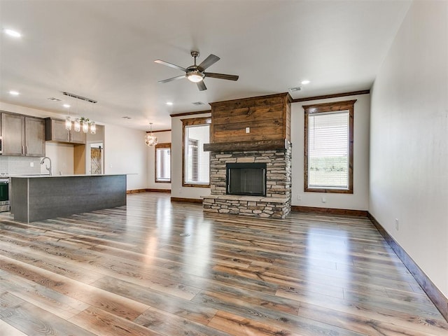 unfurnished living room featuring dark hardwood / wood-style flooring, a stone fireplace, plenty of natural light, and ceiling fan with notable chandelier