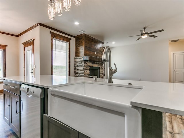 kitchen featuring dishwasher, sink, hanging light fixtures, a stone fireplace, and ceiling fan with notable chandelier