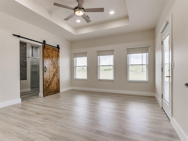 interior space featuring a raised ceiling, a barn door, ceiling fan, and light hardwood / wood-style floors