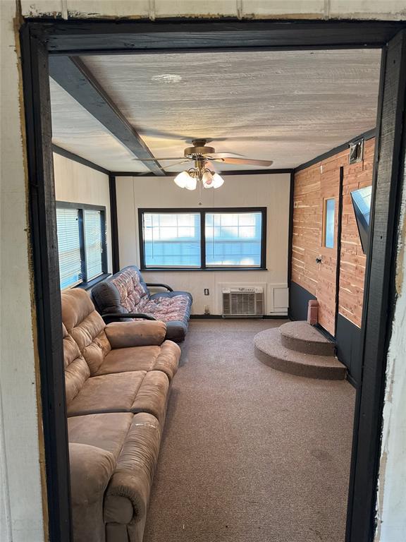 living room featuring carpet, an AC wall unit, ceiling fan, and beamed ceiling