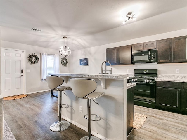 kitchen with a kitchen breakfast bar, sink, black appliances, decorative light fixtures, and a center island with sink