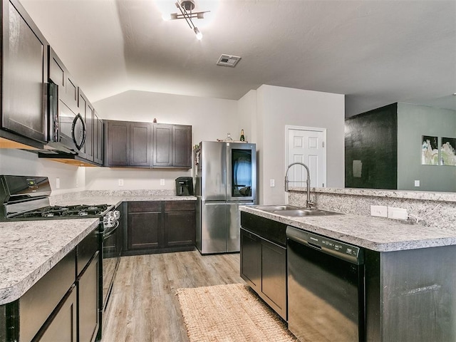 kitchen featuring light wood-type flooring, vaulted ceiling, sink, black appliances, and a center island with sink