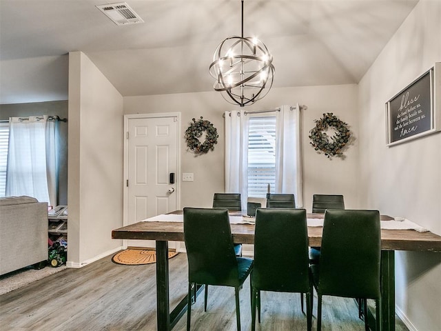 dining area with hardwood / wood-style floors, vaulted ceiling, and an inviting chandelier