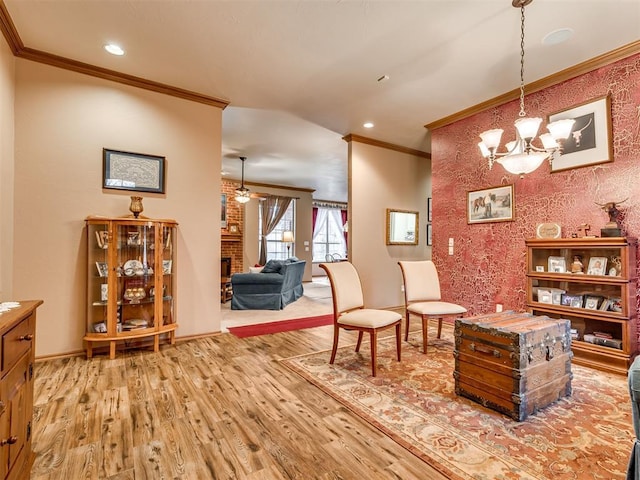 sitting room with crown molding, a brick fireplace, ceiling fan with notable chandelier, and light wood-type flooring