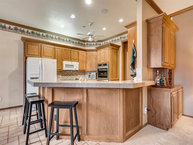 kitchen with white appliances, ceiling fan, a kitchen bar, decorative backsplash, and kitchen peninsula