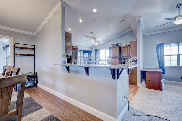 kitchen featuring a kitchen breakfast bar, light hardwood / wood-style flooring, kitchen peninsula, crown molding, and lofted ceiling