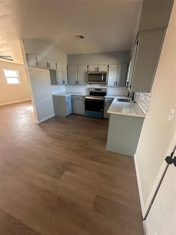 kitchen with gray cabinetry, sink, dark wood-type flooring, backsplash, and stainless steel appliances