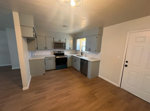 kitchen with dark hardwood / wood-style flooring, stainless steel appliances, sink, backsplash, and gray cabinetry