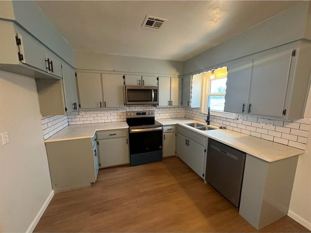 kitchen with sink, backsplash, light hardwood / wood-style floors, and appliances with stainless steel finishes