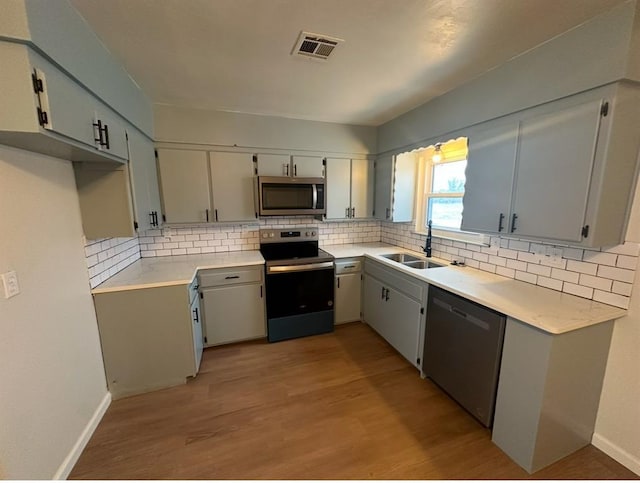 kitchen with sink, light wood-type flooring, appliances with stainless steel finishes, and decorative backsplash