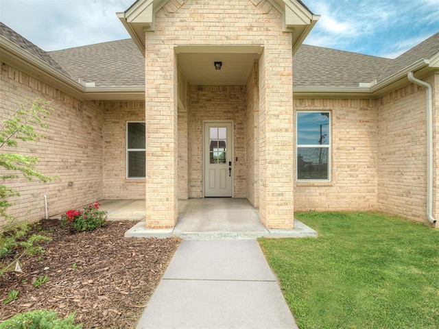 doorway to property featuring a patio area, roof with shingles, and a yard