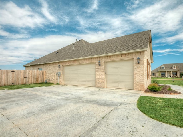 view of side of property with brick siding, roof with shingles, concrete driveway, fence, and a garage