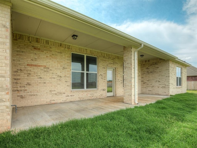 view of exterior entry with brick siding, a patio area, and a yard