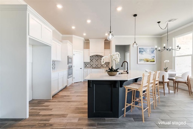 kitchen featuring light countertops, stainless steel appliances, a center island with sink, and white cabinets