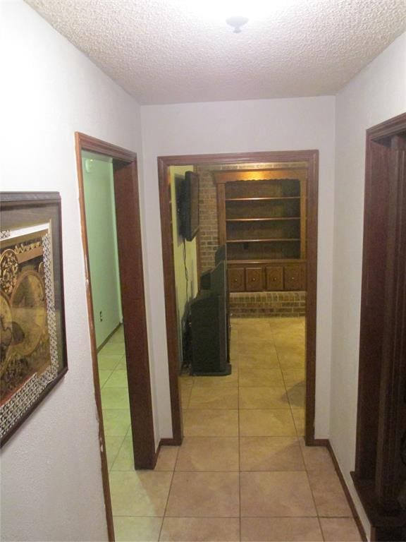 hall featuring light tile patterned floors, a textured ceiling, and built in shelves