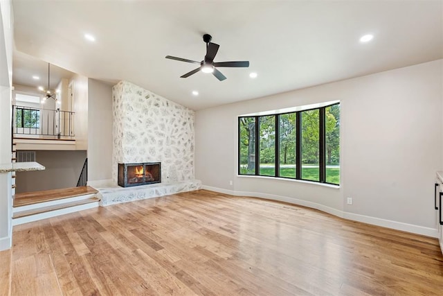 unfurnished living room featuring ceiling fan with notable chandelier, light hardwood / wood-style flooring, and a fireplace