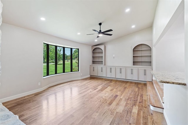 unfurnished living room with ceiling fan, built in shelves, lofted ceiling, and light wood-type flooring