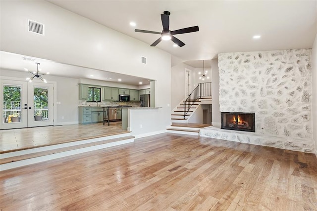 unfurnished living room with ceiling fan with notable chandelier, a large fireplace, french doors, and light wood-type flooring