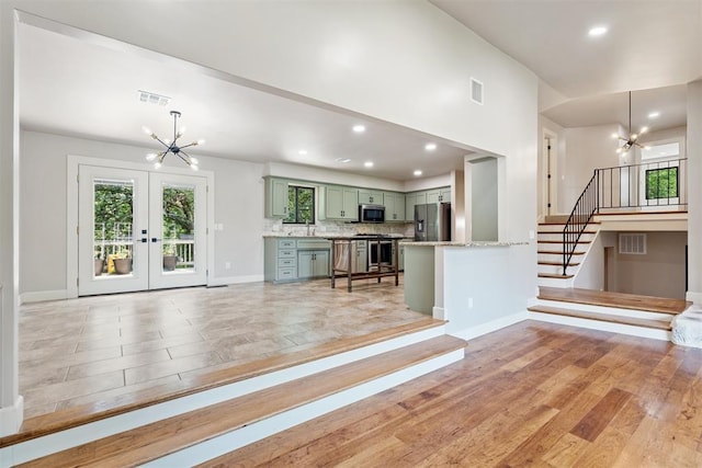 kitchen featuring pendant lighting, stainless steel appliances, an inviting chandelier, light wood-type flooring, and green cabinets