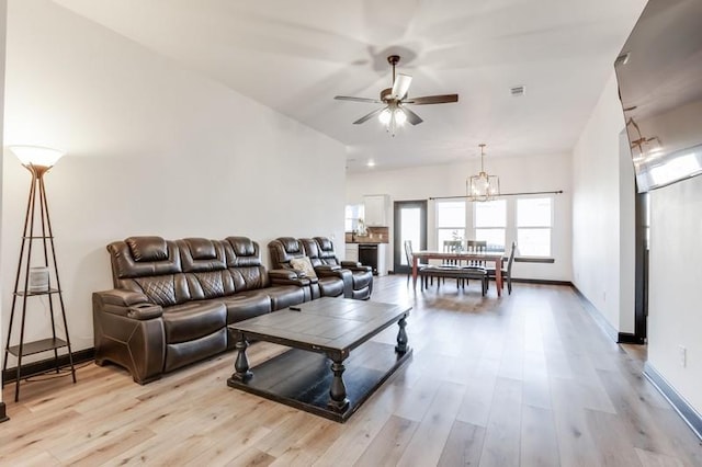 living room featuring ceiling fan with notable chandelier and light hardwood / wood-style flooring