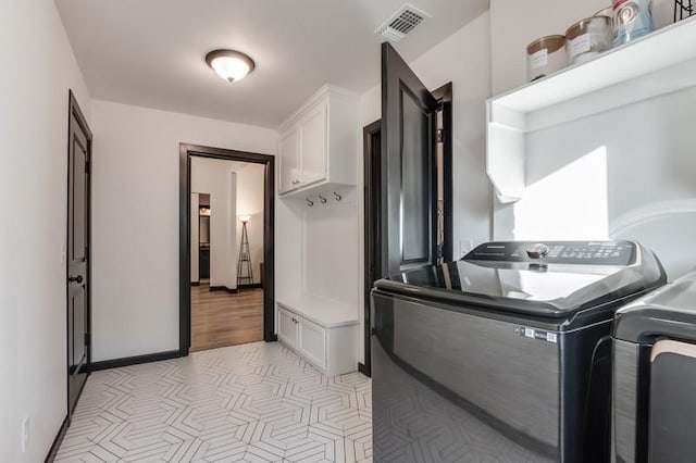 laundry room featuring washing machine and clothes dryer, light tile patterned floors, and cabinets