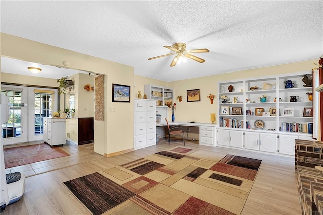 office area featuring ceiling fan, light wood-type flooring, built in desk, and a textured ceiling