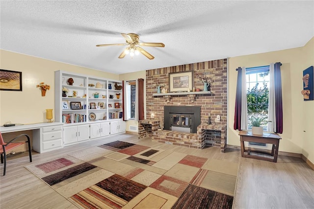 living room with ceiling fan, a brick fireplace, light hardwood / wood-style floors, and a textured ceiling