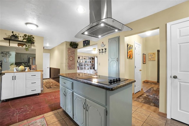 kitchen featuring a kitchen island, island range hood, white cabinets, black electric stovetop, and tile patterned floors