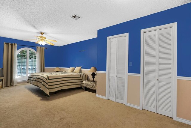 carpeted bedroom with multiple closets, ceiling fan, and a textured ceiling