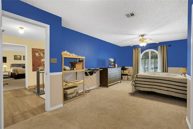 bedroom with ceiling fan, light colored carpet, and a textured ceiling