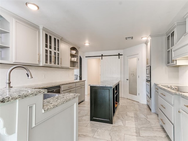 kitchen with white cabinets, a barn door, appliances with stainless steel finishes, a kitchen island, and light stone counters