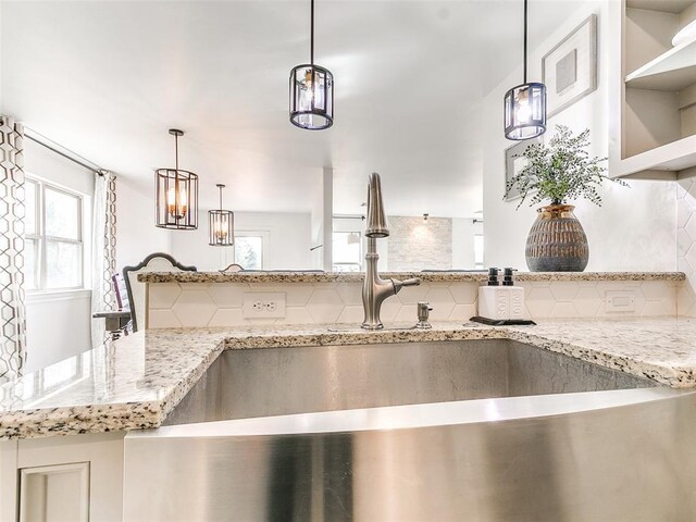 details featuring pendant lighting, tasteful backsplash, light stone counters, and sink