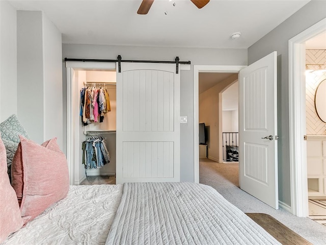 bedroom with a barn door, ceiling fan, a closet, and light colored carpet